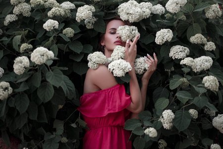 美丽的年轻时尚的女人穿着粉红色的礼服在灌木丛中的花朵