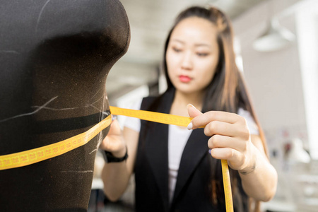 女性亚洲时尚设计师的肖像在现代阳光明媚的画室工作室中测量缝纫假人, 关注前景