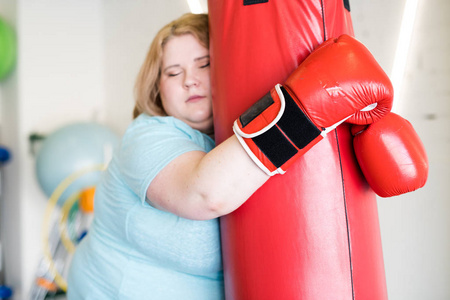 腰上的疲惫的肥胖妇女在健身房训练时斜靠打坏的画像