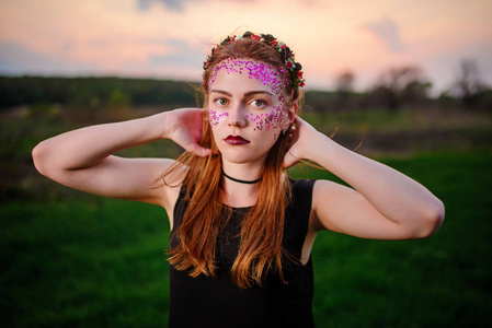 一个年轻漂亮的女人, 她的脸上有紫罗兰色的光泽, 站在草地上看着相机