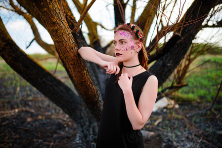 一个年轻漂亮的女人, 她的脸上有紫罗兰色的光芒, 站在一棵被烧毁的树旁