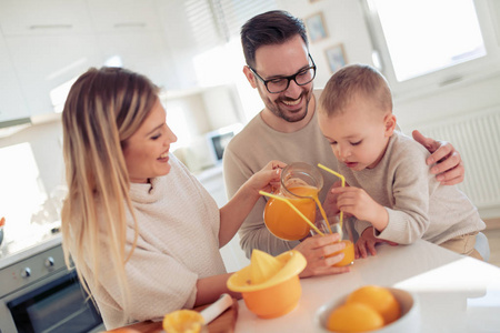 快乐的年轻家庭制作橙汁在厨房里