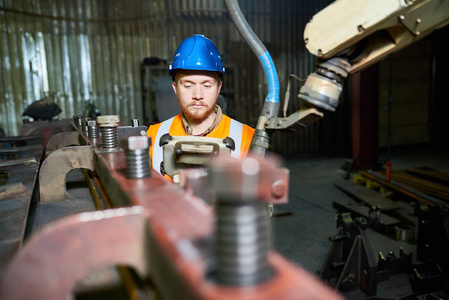 红头发胡子的机器操作员穿着反光背心和安全帽工作, 同时站在宽敞的现代工厂生产部