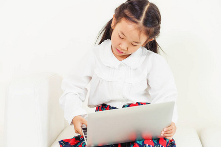 小快乐的孩子使用笔记本电脑坐在白色的沙发上。童年生活
