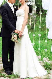 新婚夫妇站在一起, 白色的装饰品和他们身后的绿草