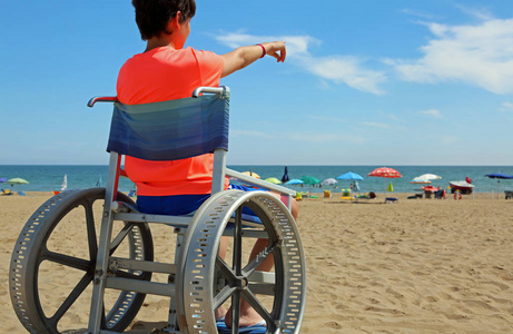 男孩在一个特别轮椅表明海的地平线在沙滩在夏天
