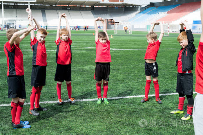 在足球练习前热身时, 一群男孩站在圆圈里做伸展运动