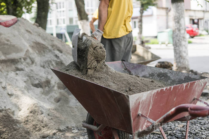 工人用铲子把手推车装满沙子用来建造人行道建筑工具铲和推车在轮子与