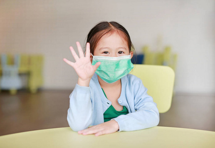 可爱的亚洲小女孩戴着保护面具, 在儿童房的儿童椅子上显示有五个手指