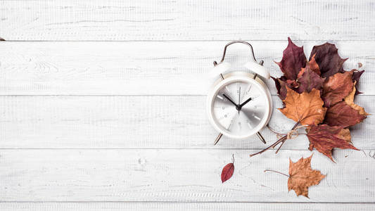 老式闹钟和秋天掉落的枫叶在白色木桌的背景下, 平躺, 顶视图。复制文本的空间