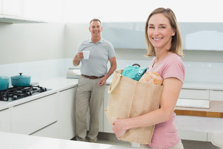 携带杂货袋边咖啡杯在厨房里的男人的女人