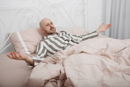 英俊的秃头, 有胡子的男人在条纹睡衣是躺在床上, 考虑枕头和粉红色床上用品