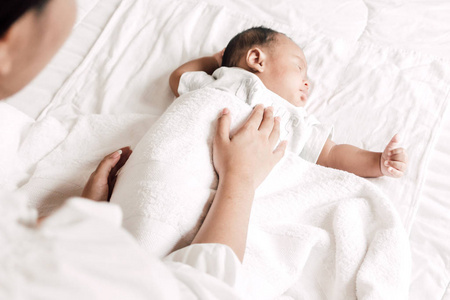 母亲抱着熟睡的婴儿手在白床上。对家庭概念的爱