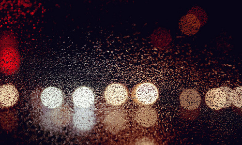 城市道路通过雨在汽车挡风玻璃上看到夜间。重点放在一些水滴上