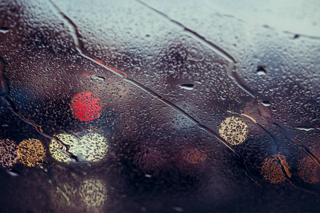 穿过雨落在汽车挡风玻璃上的城市道路。焦点在一些水滴上