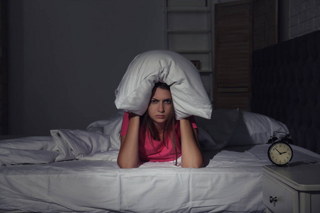 在家里的床上用枕头捂头的年轻女子。睡眠障碍