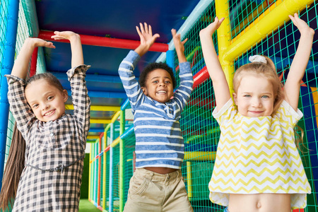 腰上的三快乐的孩子跳举手, 而在玩区域的乐趣和看着相机的肖像