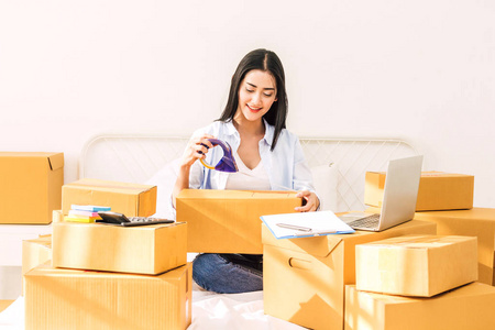 年轻女子自由职业者工作中小型企业在线购物和包装纸板箱在床上的家庭企业在线送货和送货概念