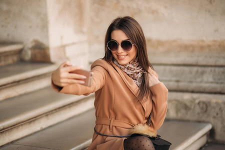 戴墨镜的漂亮女孩用智能手机拍照。自拍