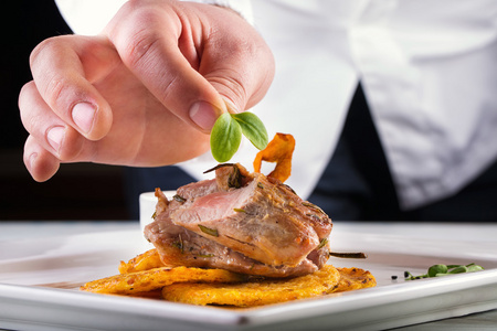厨师在酒店或餐厅厨房做饭，只手。预先准备的肉牛排配土豆或芹菜煎饼