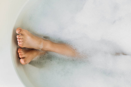 泡沫浴缸中美丽女性腿的部分视图