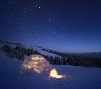 夜风景与雪屋与光。极端的房子。冬天在山里。天空与星星