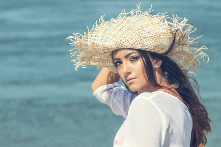 在海滩上戴着夏日帽子的美丽年轻女子的画像。特写肖像女孩用草帽