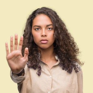 年轻的西班牙裔商业妇女做停止唱歌与手掌的手。脸上带有否定和严肃手势的警告表达式