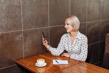 微笑的女商人坐在咖啡馆里, 使用智能手机