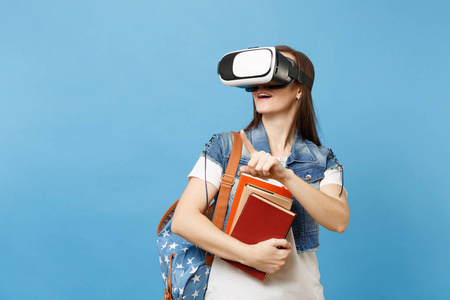 虚拟现实中的年轻女性学生眼镜拿着书摸像按按钮的东西, 指向在蓝色背景上孤立的浮动虚拟屏幕。学校大学教育