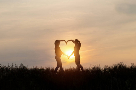 女性手在日落的背景上显示心脏标志