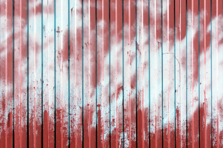 从波纹金属栅栏。表面涂上红色和浅蓝色。油漆斑点。空背景