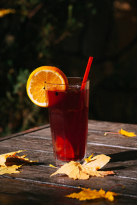 木桌上的一杯热饮料和秋叶。在大杯子的热葡萄酒与阳光和阴影外