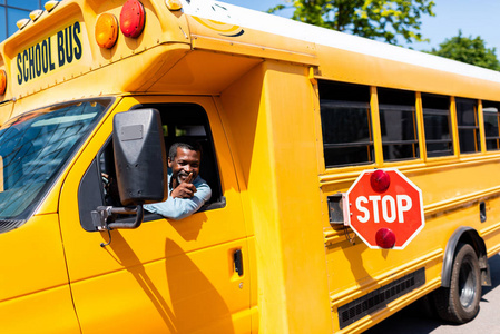 微笑成熟的非洲裔美国人公共汽车司机看窗外和手势