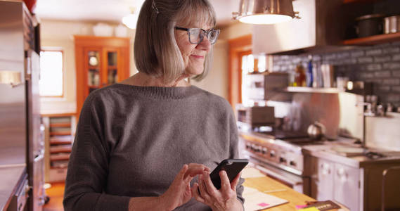愉快的资深妇女在家庭厨房环境中发送短信