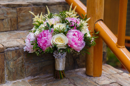 婚礼配饰。新娘在石头楼梯上的粉红色牡丹和白玫瑰的花束