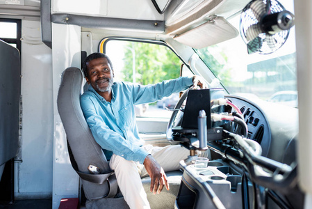 微笑成熟的非洲裔美国人公共汽车司机坐在公共汽车上看相机