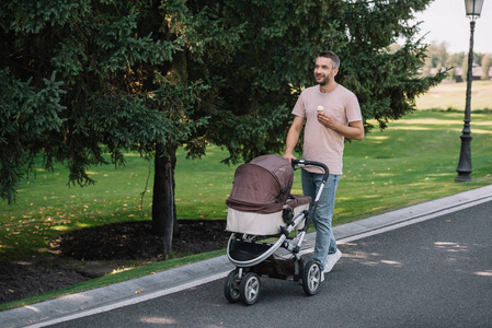 微笑的父亲散步与婴儿马车和冰淇淋在公园里, 看着远离