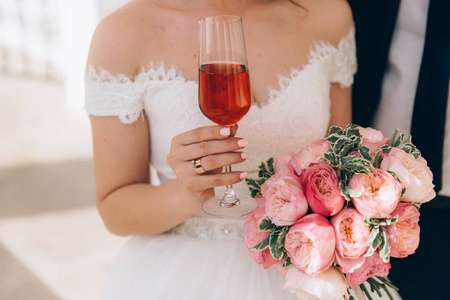 在她手里拿着一束粉红色的牡丹花, 一杯粉红色的香槟, 戴着一个扁平的订婚金戒指。新娘修指甲