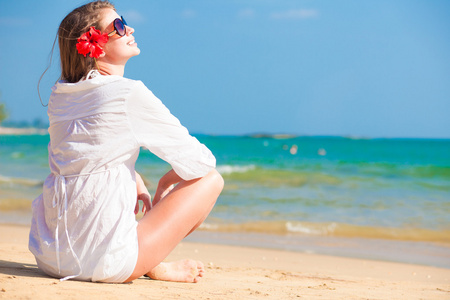 回观年轻长发女子穿着白衬衣，太阳镜花在坐在海滩上的头发