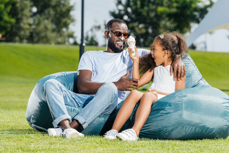 非洲裔美国人的女儿玩冰淇淋, 而坐在与父亲的豆子袋椅