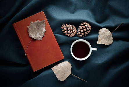 秋冬的气氛。一杯茶, 干树叶, 松树锥在黑色的床单上。顶部视图。平躺