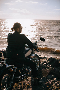 英俊的车手坐在古典摩托车附近在海与后面光