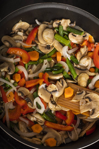 在黑底煎锅里用蘑菇搅拌蔬菜。烹调食物。从上面查看