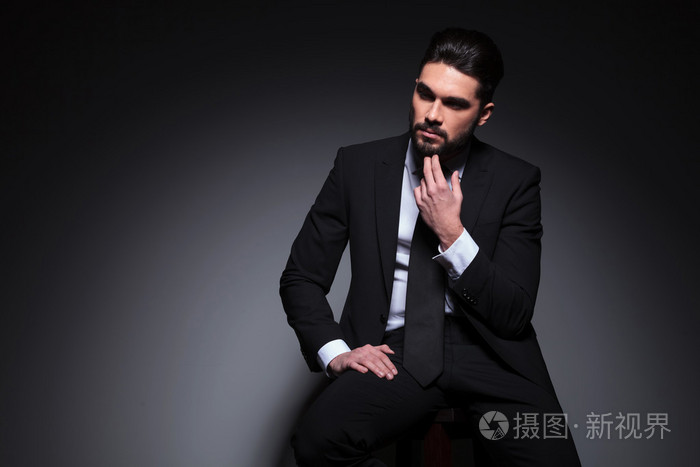 沉思的时尚男人坐在凳子上,看起来带走