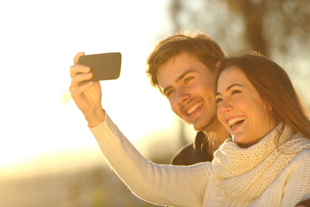夫妇在日落时分与智能手机拍照合影