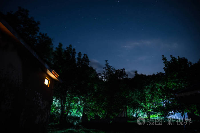 晚上在森林里建筑的山夜风景与月亮或老式乡下房子在晚上与云彩和星.