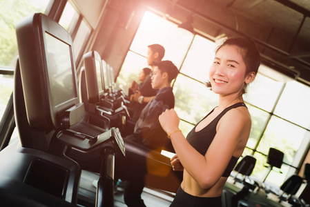 愉快的亚洲妇女与一群年轻人跑步或慢跑在跑步机在现代体育健身房。运动和运动概念