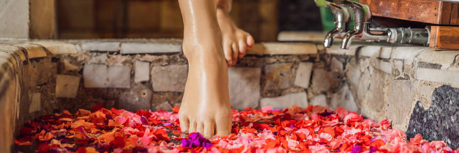 妇女的脚的作物看法在浴与热带花和芳香油的花瓣