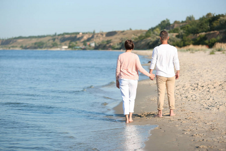 快乐的成熟夫妇在阳光明媚的日子在海滩漫步